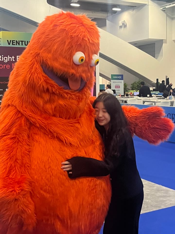 Suyeon hugging a big fuzzy orange mascot at a conference